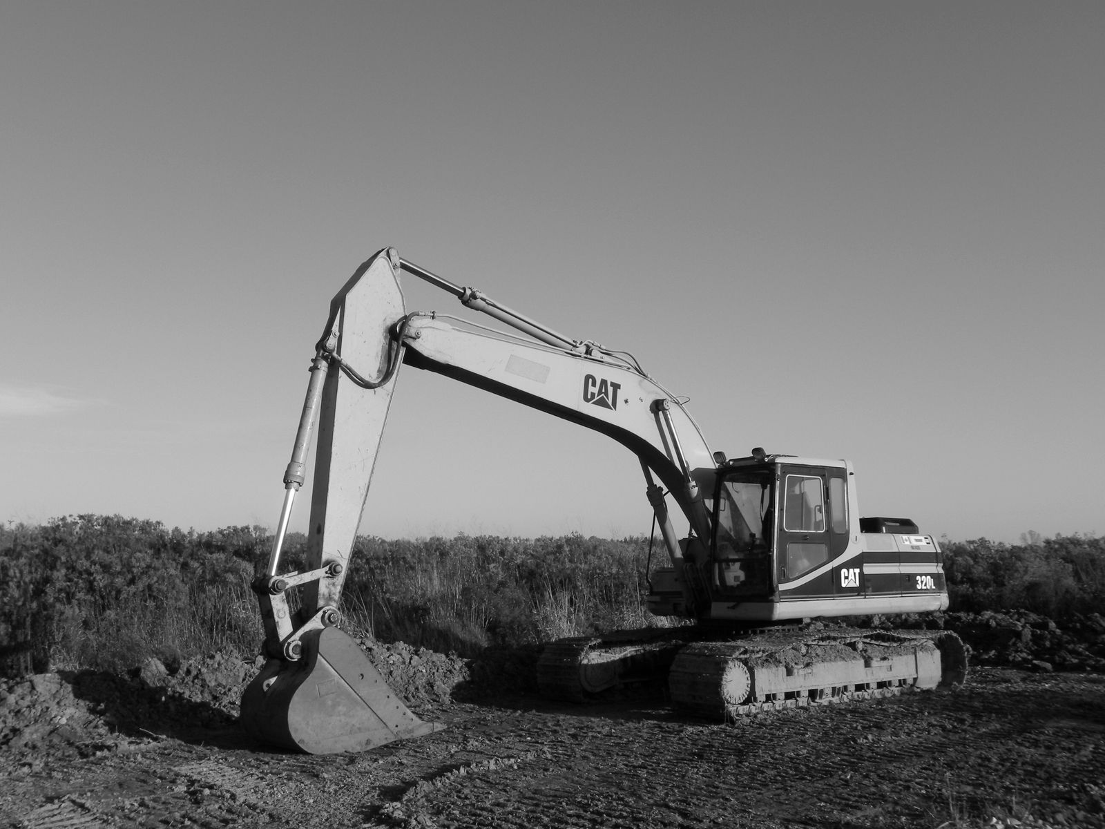 A tracked excavator standing on cleared ground, in black and white.